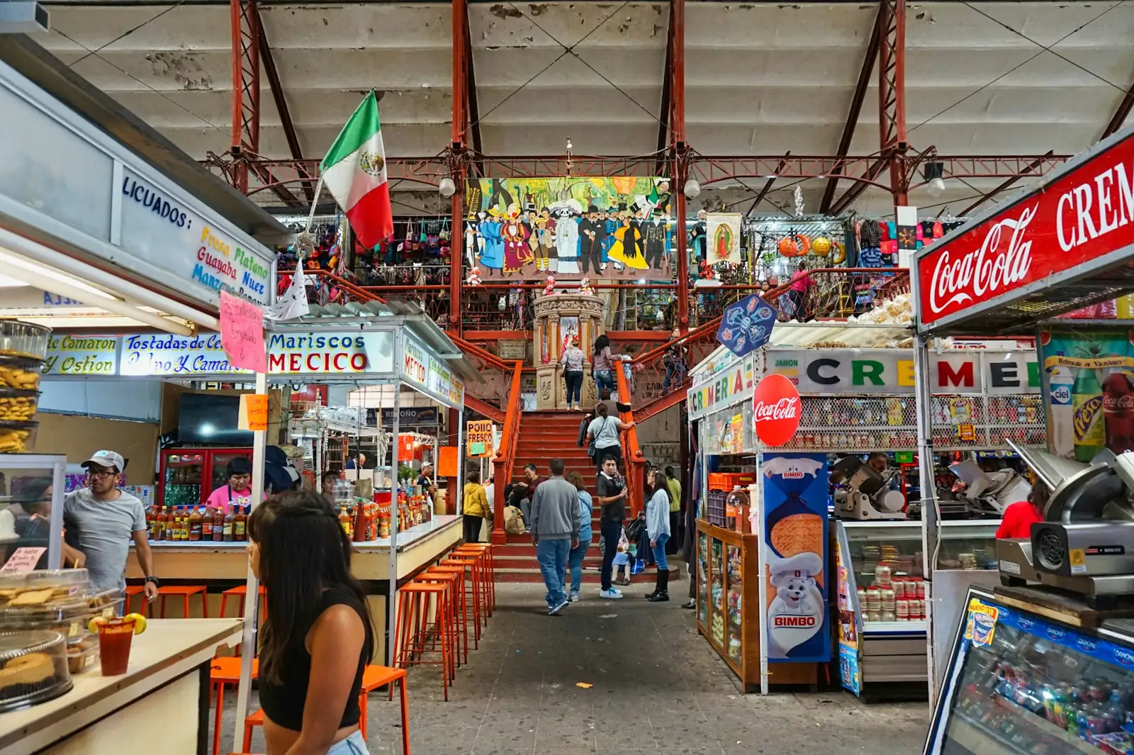 Pasillo de un mercado con puestos de comida y abarrotes, gente comprando
